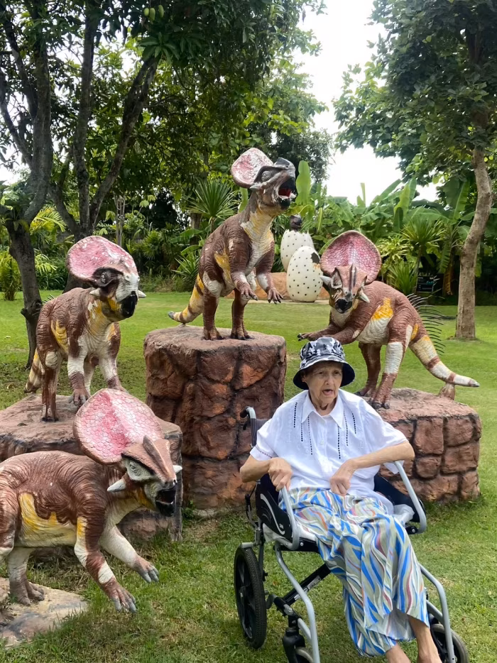 Children in costume beside a resident in a wheelchair, near the dinosaur statues.