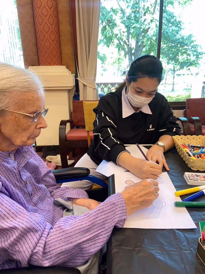 A resident and carer with craft materials at a table.