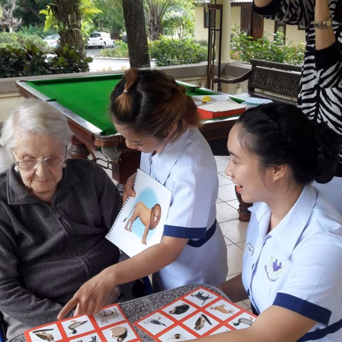 A carer teaching residents a table game near the pool table.