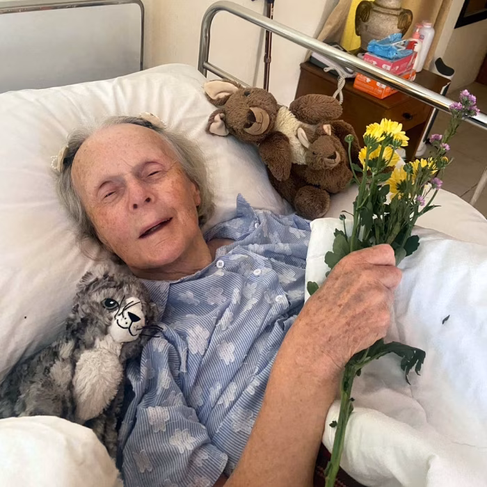 A resident in bed, holding flowers, with a carer nearby.