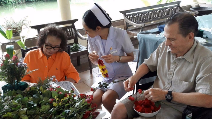 Residents and a carer arranging flowers at a table.