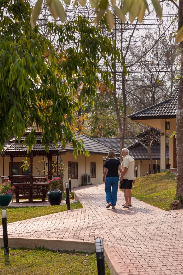Two figures walking a garden path near a Thai-style pavilion.