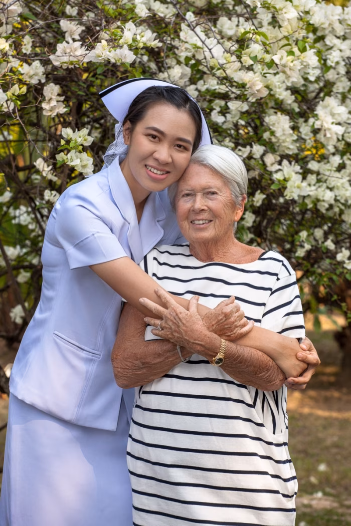 A carer embracing a resident in the garden, among white flowers.