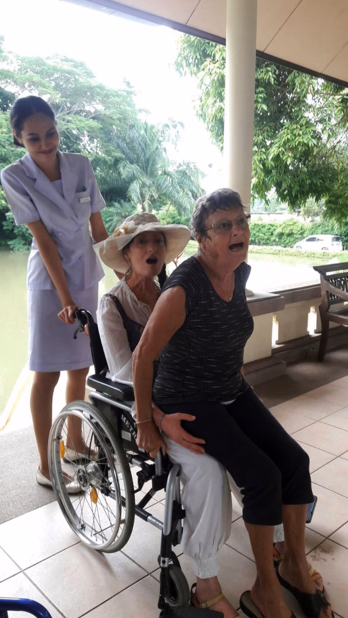 A carer pushing a resident's wheelchair along the covered walkway.