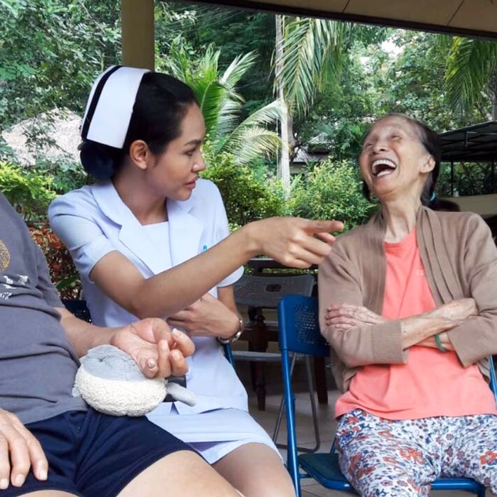 A carer helping a resident with a beading activity, both laughing.