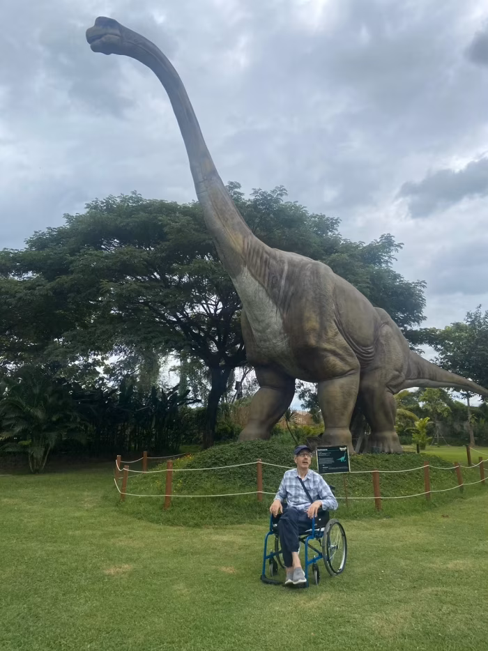 A resident in a wheelchair beside the resort's dinosaur statue.