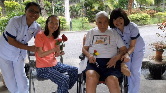 A carer presenting a rose to two seated residents.