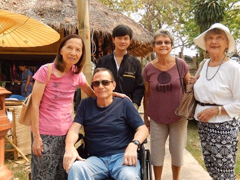 Four residents and visitors posing together near a thatched structure.