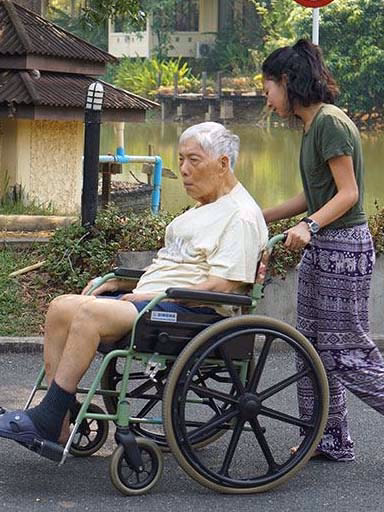 A carer helping a resident in a wheelchair beside the lake.