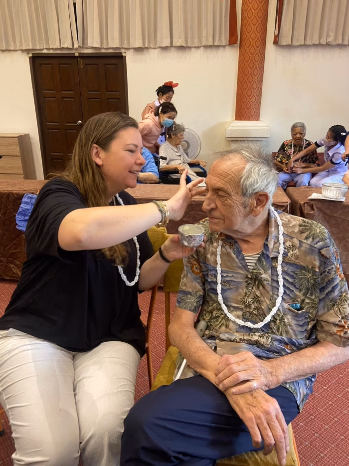 Staff placing a garland on a resident, with talcum powder blessing.