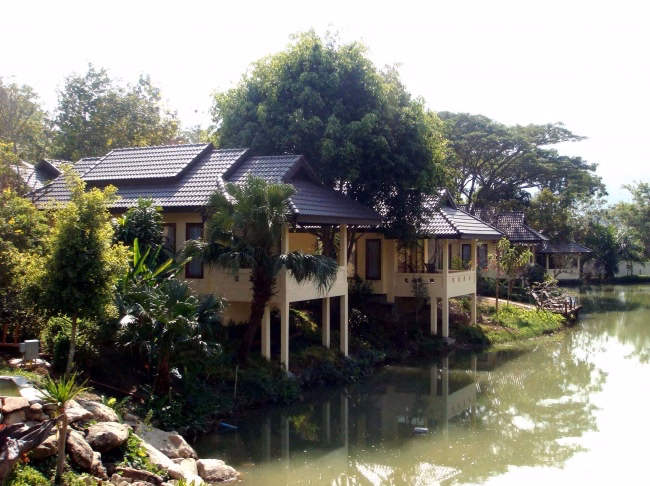 Villas on stilts at the edge of the resort lake, under mature trees.
